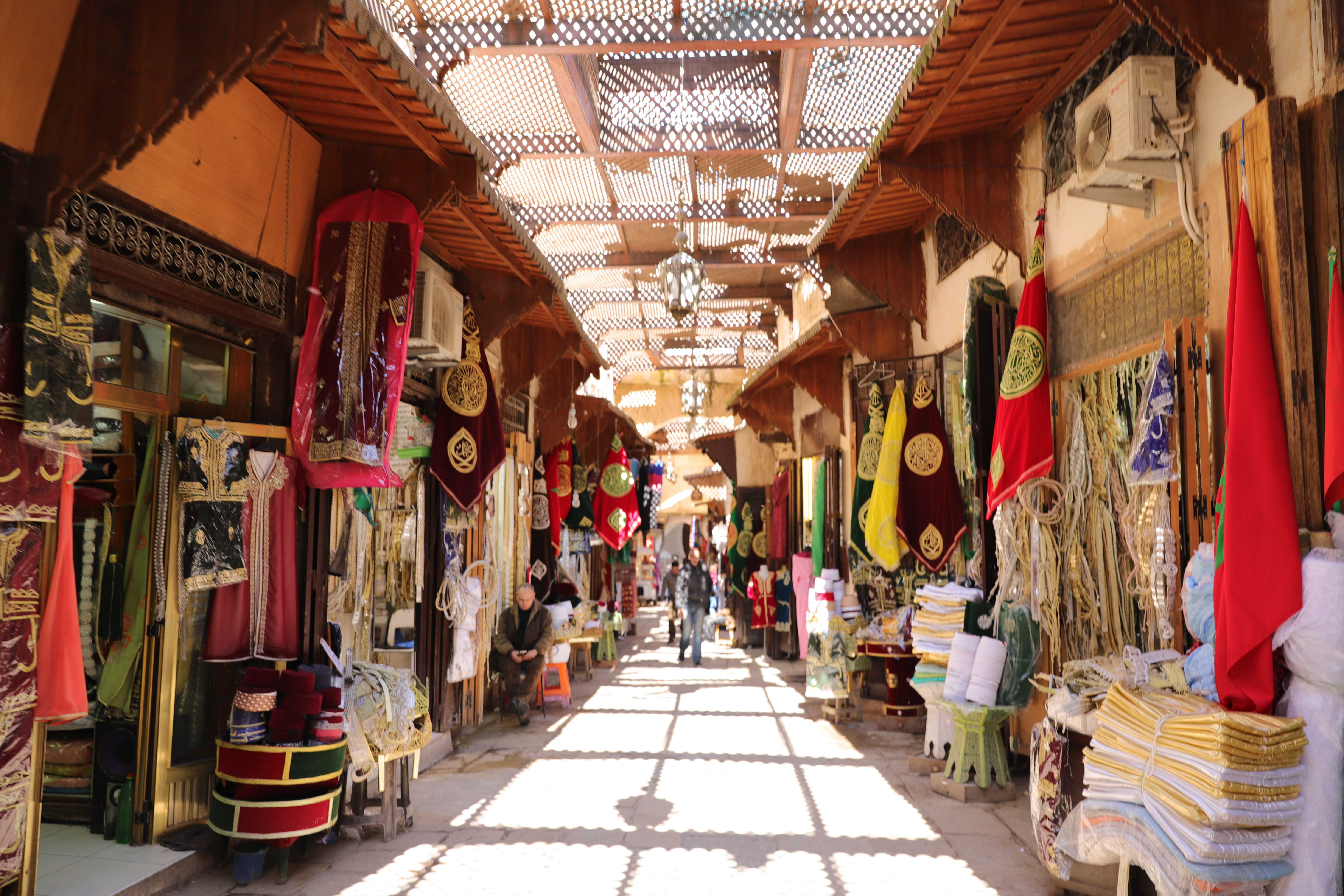 Überdachte Souk-Gasse mit Stoffen und Gewändern in der Medina von Fès